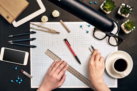 Office desk background hand with pen writing construction project ideas concept. With tablet, drawing equipment and a cup of coffee. View from aboveの写真素材
