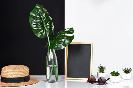 The stylish interior with mock up poster frame, leaves in glass bottle on table with black and white wall on background. The minimalism concept of space. Copy spaceの写真素材