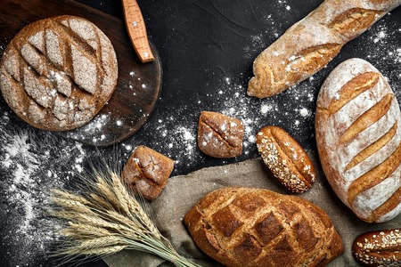 Homemade rye bread sprinkled with flour and various grains and seeds on a black background with spikelets of wheat or rye and oats. Top view. still life. Copy space. flat layの写真素材