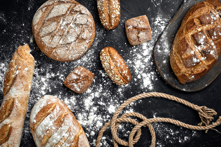 Homemade rye bread sprinkled with flour and various grains and seeds on a black background with...