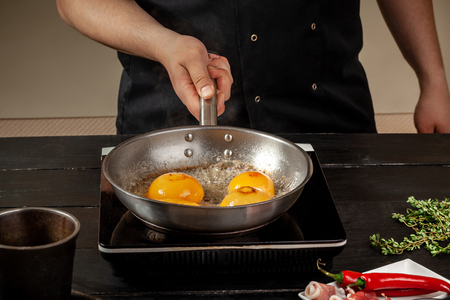 Peaches on a fry pan. Canned fruit yellow peaches, black wooden background, board.の写真素材