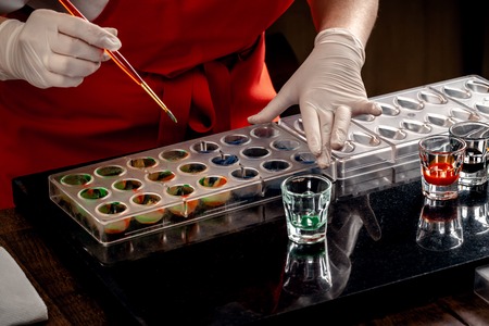 Woman a confectioner in red uniform and white gloves doing candy in special shapes from dairy chocolate with edible paint.の写真素材