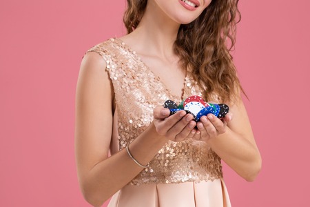 Woman holding a gambling chips in her nands on pink background. Close-upの写真素材