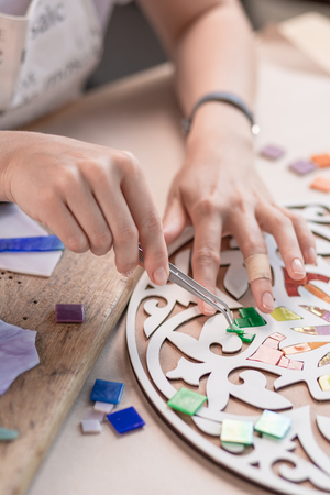 Workplace of the mosaic master: womens hands holding tool for mosaic details in the process of making a mosaicの写真素材