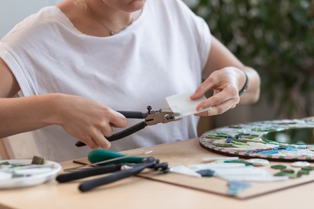 Workplace of the mosaic master: womens hands holding tool for mosaic details in the process of...