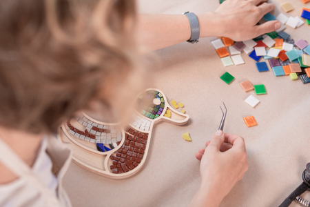 Workplace of the mosaic master: womens hands holding tool for mosaic details in the process of making a mosaicの写真素材