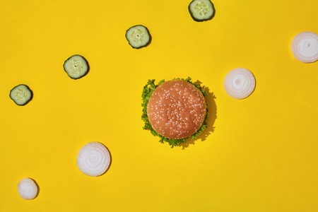 Tasty fresh unhealthy hamburger with ketchup and vegetables on yellow vibrant bright background. Top View with Copy Space.の写真素材