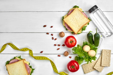 Lunch boxes with sandwiches and fresh vegetables, bottle of water, nuts and eggs on white wooden background. Top view with copy spaceの写真素材