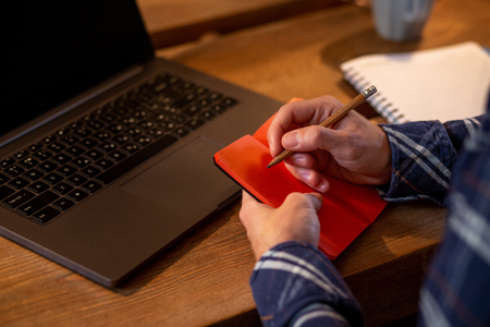 Cropped image of casual business man or freelancer planning his work on notebook, working on laptop computer with smart phone, cup of coffee on table at coffee shop or home office.の写真素材