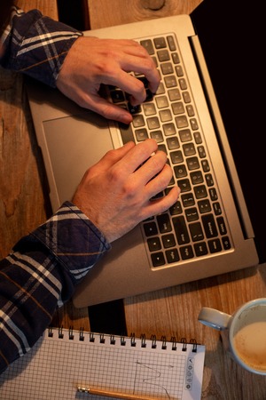 Young man drinking coffee in cafe and using laptop. Mans hands using laptop during coffee breakの写真素材