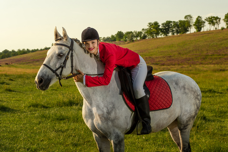 Young woman rider, wearing red redingote and white breeches, with her horse in evening sunset light.の写真素材