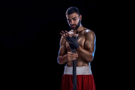 Boxer preparing her gloves for a fight. Photo of muscular man strapping up hands on black background.の写真素材