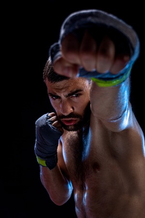 The boxer is ready to deal a powerful blow. Photo of muscular man with strong hands and clenched fists in blue stripes on black background.の写真素材