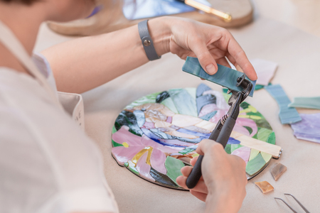 Hands of master working on new modern colorful mosaic. Close-up. Workshop. Workplaceの写真素材