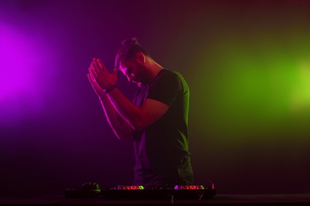 DJ at work mixing sound on her decks at a party or night club with colourful smoke light background