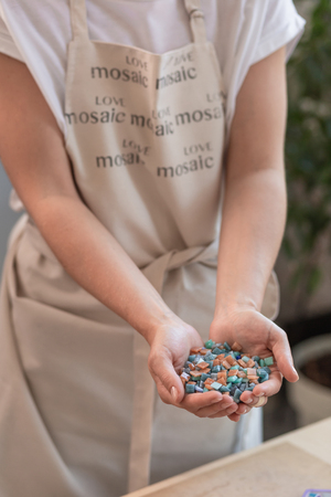 Workplace of the mosaic master: womens hands holding mosaic details in the process of making a...