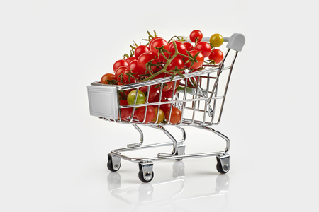 Mini shopping cart full with cherry tomatos on white background. Copy spaceの写真素材