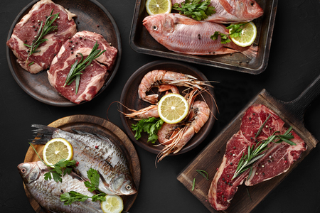 Assortment of fish, meat, beef steak and shrimp. Healthy protein source and body building food on black background. Top view, flat lay. Still lifeの写真素材