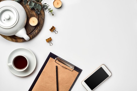 Notebook with craft paper, mobile phone, black tea, glasses on white background with copy space.の写真素材