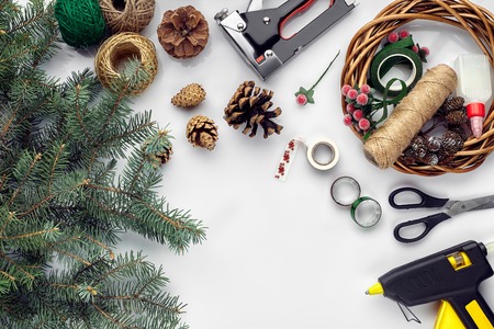 Preparing for Christmas or New Year holiday. Flat-lay of fur tree branches, wreaths, rope, scissors, craft paper over white table background, top view.の写真素材