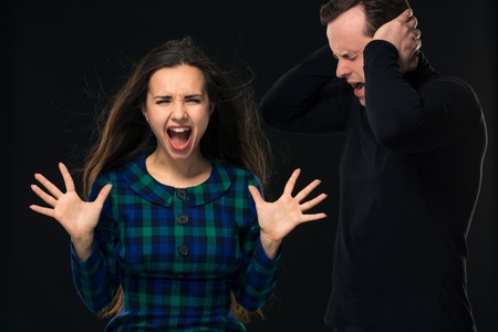 ouple having conflict, bad relationships. Angry fury woman screaming man closing his ears on black backgroundの写真素材
