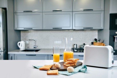 Toaster with fresh toast, eggs and glass of orange juice on a light kitchen tableの写真素材