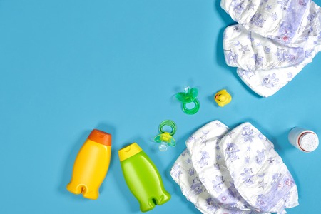 Baby care with bath set. Nipple, toy, diapers, shampoo on blue background top view mockupの写真素材
