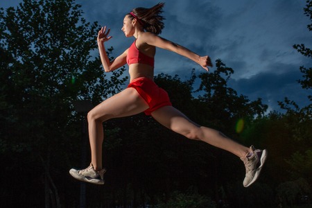 Young happy woman running outdoor in a city park. Girl running running in the nature to lose weight and maintain a healthy life.の写真素材