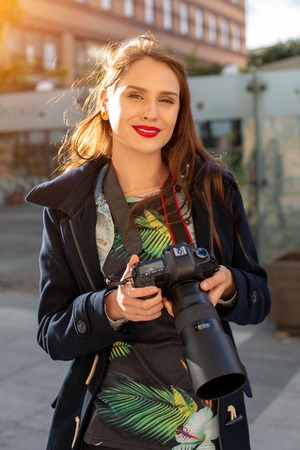 Portrait of professional female photographer on the street photographing on a camera.