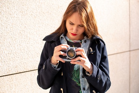 Happy hipster girl making photo with retro camera on city streetの写真素材