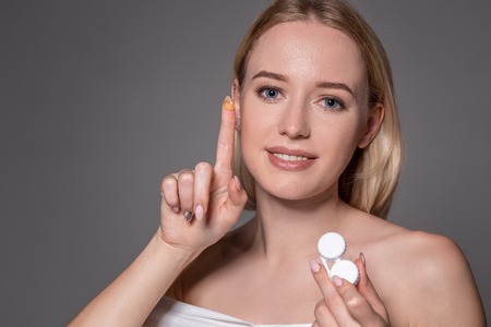 Portrait of young beautiful woman with natural makeup and contact eye lens in hand. Close-up of female model holding white lens box.の写真素材
