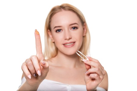 Focus on contact lens on finger of young woman. Young woman holding contact lens on finger in front of her face. Woman holding contact lens on white background.の写真素材