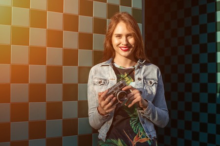 Cool funny girl model with retro film camera wearing a denim jacket, dark hair outdoors over city...