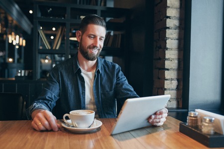 Young man drinking coffee in cafe and using tablet computerの写真素材
