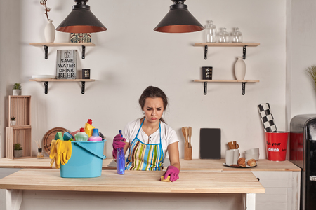 Beautiful cheerful brunette woman in gloves cleaning modern kitchenの写真素材