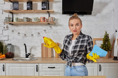 Professional young woman wearing rubber protective yellow gloves holding bottle cleaners in the kitchen.の写真素材