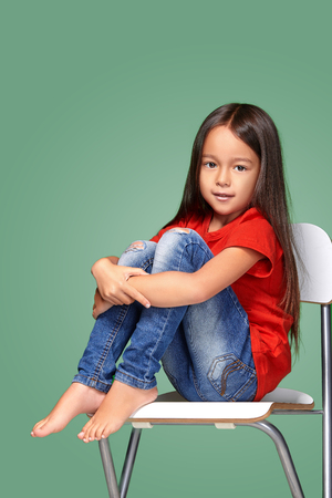 little girl wearing red t-short and posing on chairの写真素材