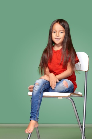 little girl wearing red t-short and posing on chairの写真素材