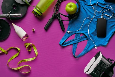 Health fitness background. Sneakers, dumbbell, power grip, green apple, water bottle, blue shirt, phone and earphone on dark background. Top view. Copy spaceの写真素材
