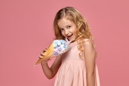 Little girl with a blond curly hair, in a pink dress is posing with an ice-creamの写真素材