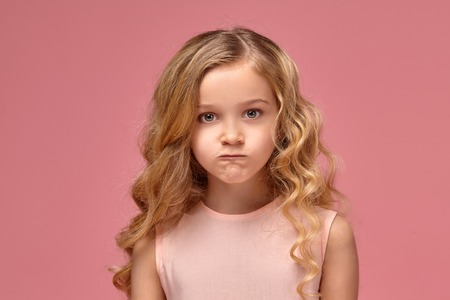 Little girl with a blond curly hair, in a pink dress is posing for the camera