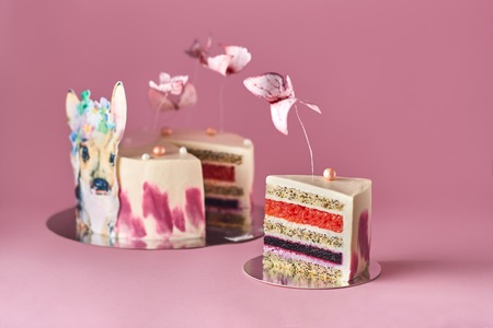 Pastel colors tasty cake with butterflies and little deer. White, yellow, pink and blue cream custard. Pink background. Selective focus.の写真素材