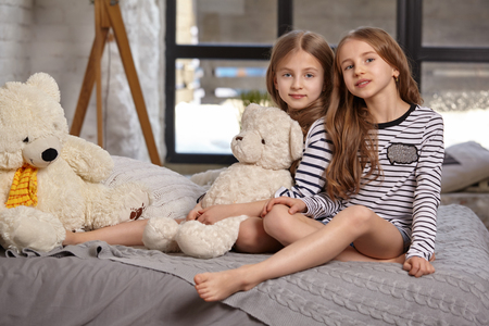 The image of two little sisters sitting on the bed in the room.の写真素材