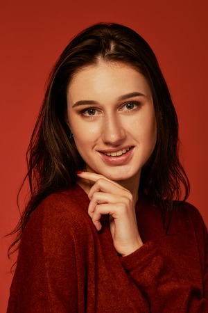 Close up portrait of cute and young smiling brunette. Studio photo on red background