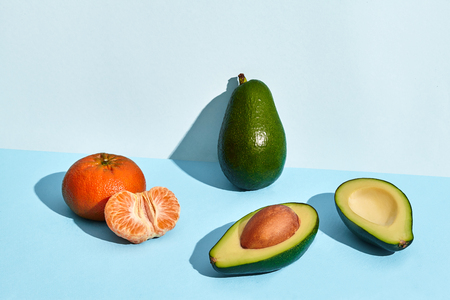 Composition of fresh fruits, mandarin, whole avocado and two halfs of cutted avocado on two-colored...