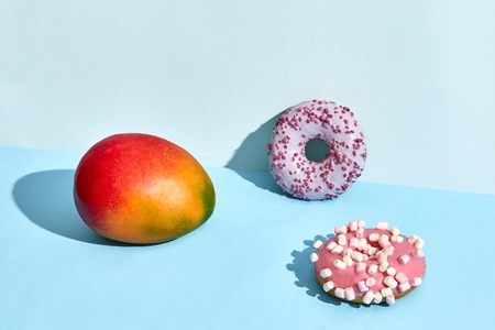 Composition of fresh fruits and sweets, two donuts and juicy mangoの写真素材