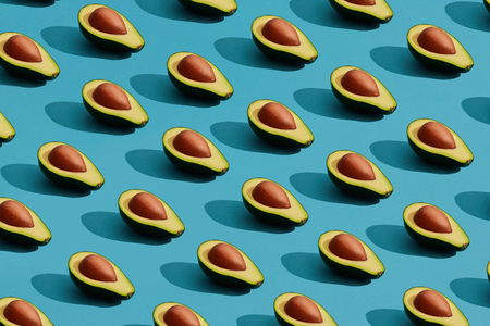 Colorful fruit pattern of fresh cutted avocado halves with pits on blue pastel backgroundの写真素材