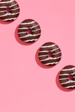 Food design with tasty chocolate glazed donut with white strips on coral pink pastel background top view patternの写真素材