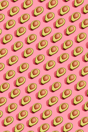 Colorful fruit pattern of fresh cutted avocado halves with pits on coral pink background, top viewの写真素材