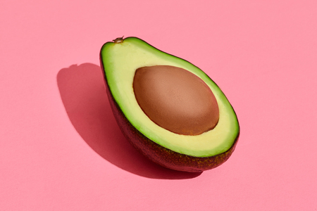 Colorful fruit pattern of fresh cutted avocado halve with pit on coral pink background, top viewの写真素材